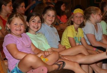 Campers sitting together on wooden benches inside a building at Athens YMCA Camps