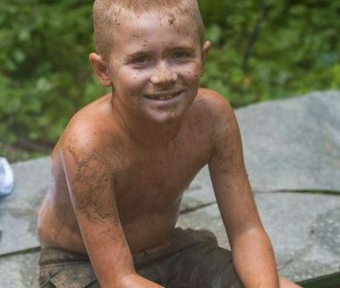 Camper sitting outdoors covered in mud at Athens YMCA Camps
